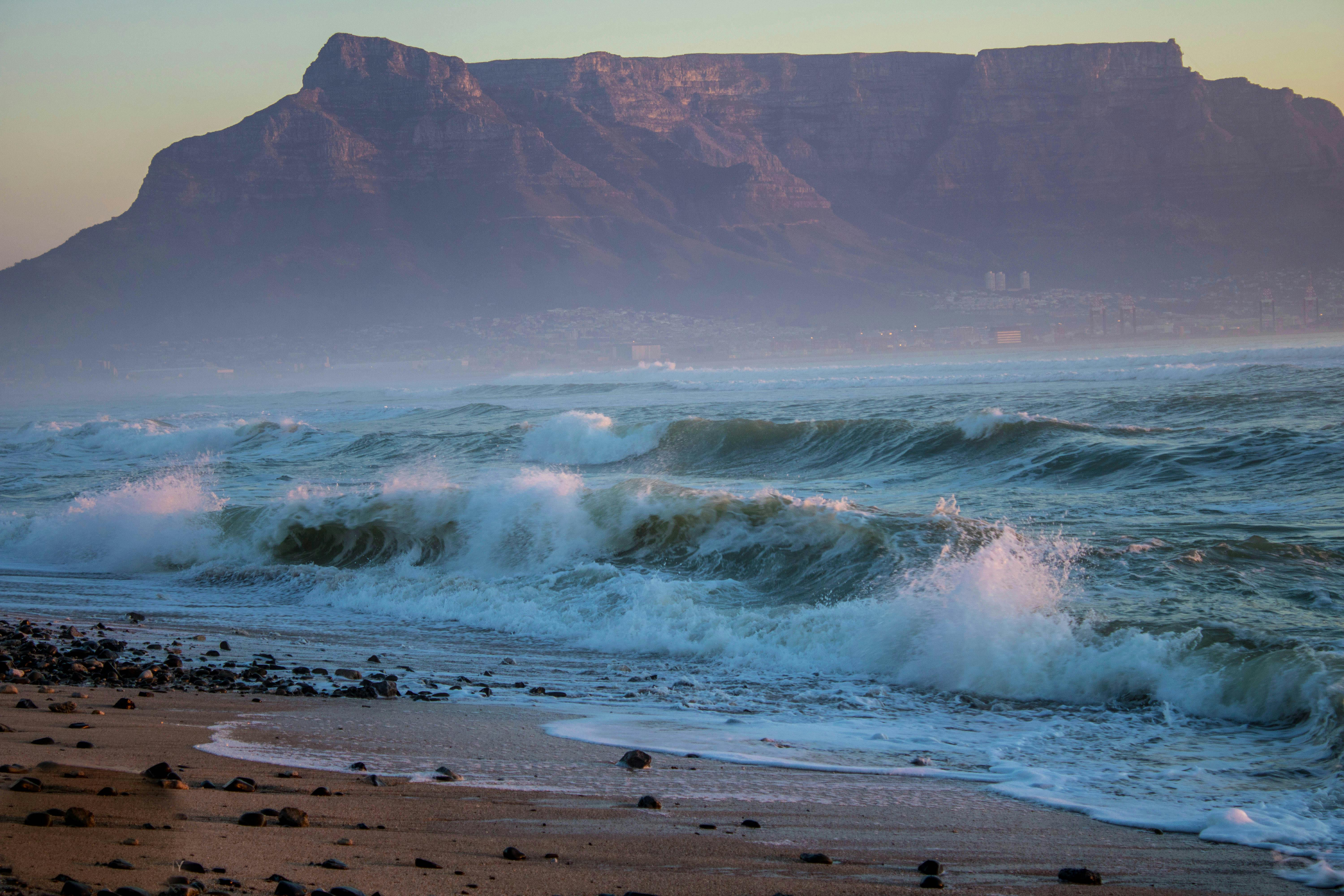 Stunning view of waves crashing on the shore with Table Mountain in the background at Cape Town, South Africa.