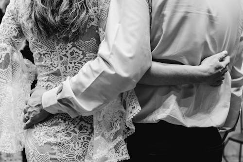 Black and white crop anonymous bride and groom wearing chic gowns embracing each other with tenderness during romantic wedding celebration