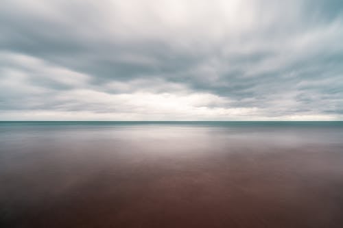 Long exposure scenery of dramatic cloudy sky over tranquil blue sea on overcast weather