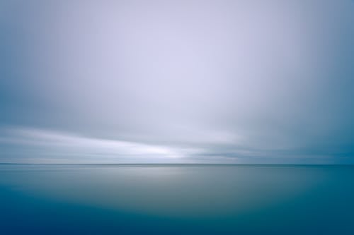 Long exposure scenic shot of endless tranquil sea with clean turquoise water beneath majestic cloudy sky