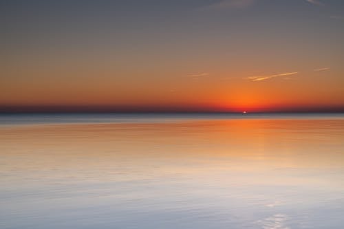 Magnificent scenery of tranquil sea beneath picturesque sunset sky and reflecting bright red sunlight