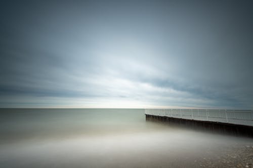Long exposure picturesque view of wooden pier near calm rippling sea under majestic cloudy sky in evening