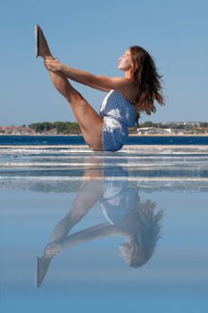 Side view of concentrated young fit female traveler with long hair performing Urdhva Mukha Pascimottanasana pose during yoga session on seashore against blue sky