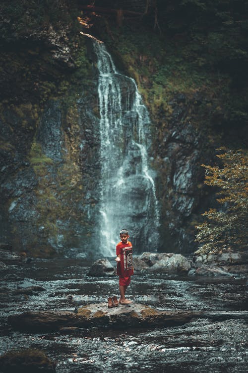 A Boy Sanding on a River Rock