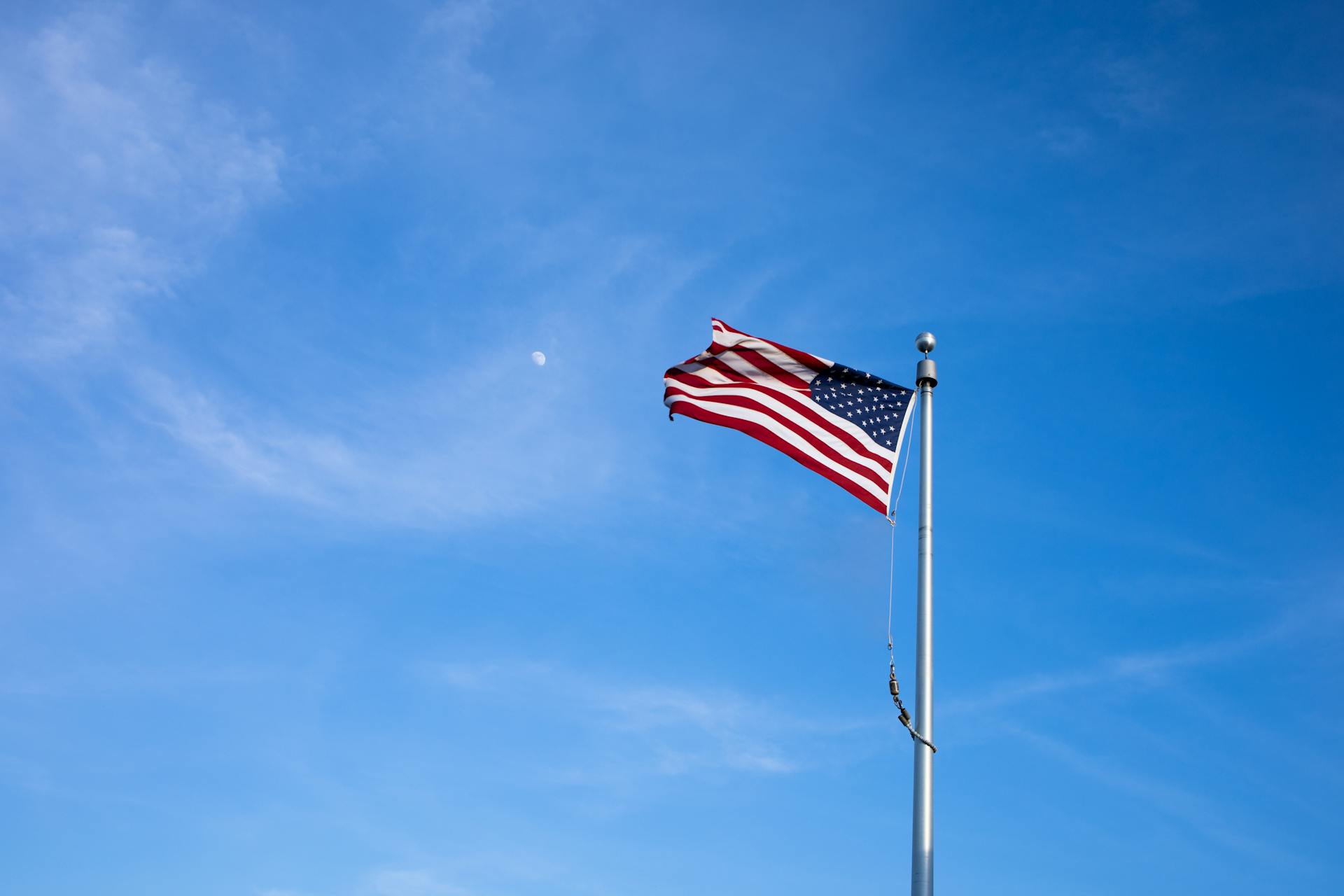 An American flag on a high pole waving against a bright blue sky during the day.