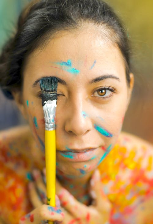Pensive woman dyeing eyebrow with paintbrush