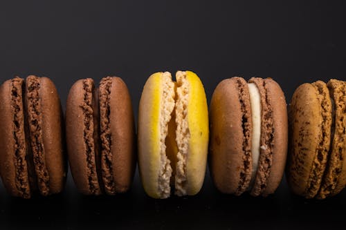 Top view of yummy sweet macaroons with cream arranged in row on black background