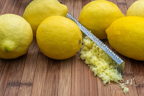 High angle of fresh ripe lemons and zest placed near grater on wooden table
