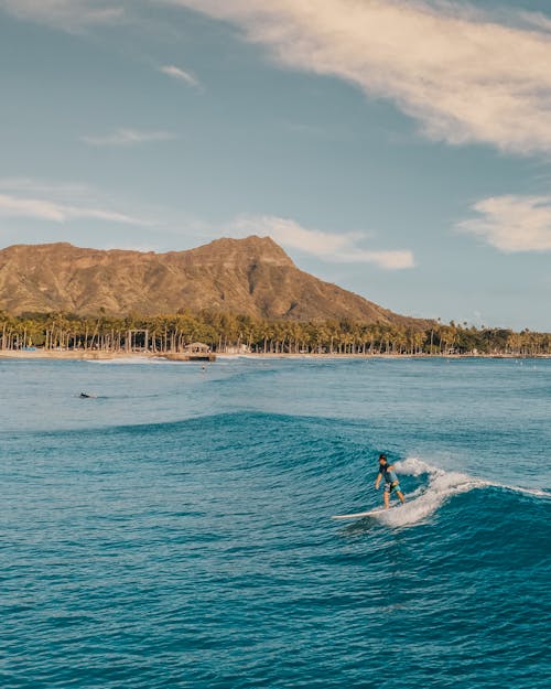 Person Surfing on Sea Near Mountain