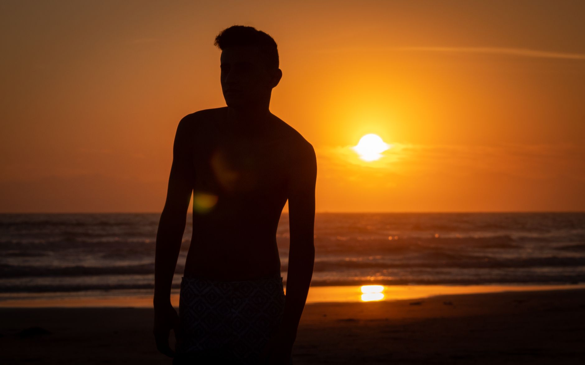 Silhouette of a man on a beach at sunset, capturing a dramatic and serene seascape.