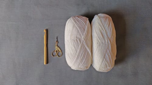 Two White Yarn Roll Beside Gold Scissor