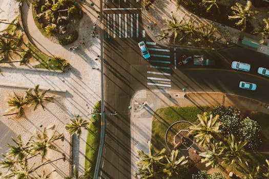 A scenic aerial shot of a Hawaiian street intersection with palm trees, cars, and pedestrian activities.