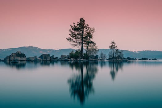Tranquil sunset over Lake Tahoe with islets, trees, and mountain reflections.