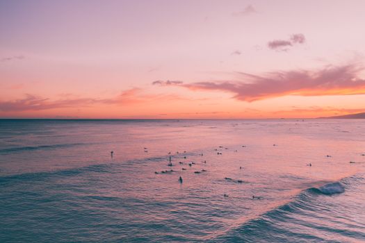 夏威夷日落时分，冲浪者在宁静的海洋和柔和的天空下，构成一幅宁静的场景