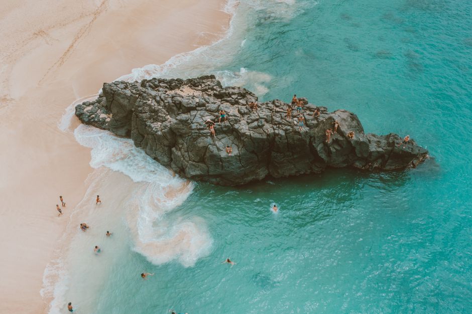 Stunning Kohala Waterfalls with Exclusive Landing Helicopter Tour Review Review 2026 - People enjoying rock jumping at Waimea Bay, Hawaii with turquoise ocean waters and sandy beach.