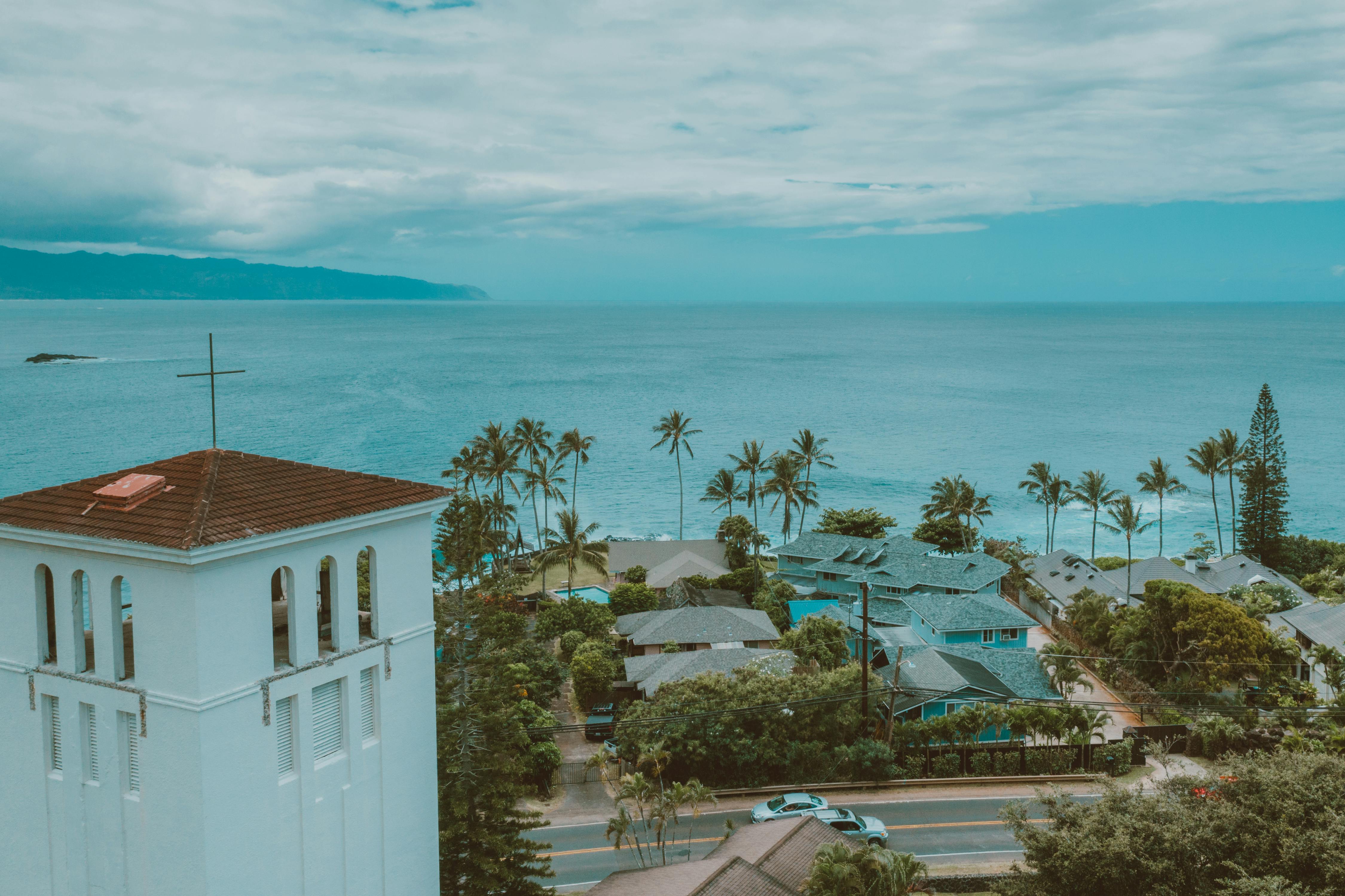 Aerial view of Oahu's scenic coastline with a church tower, palm trees, and ocean backdrop.