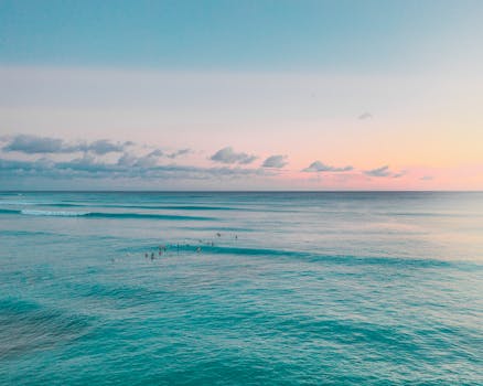Aerial view of a beautiful Hawaiian sunset over a tranquil ocean with surfers enjoying the waves.