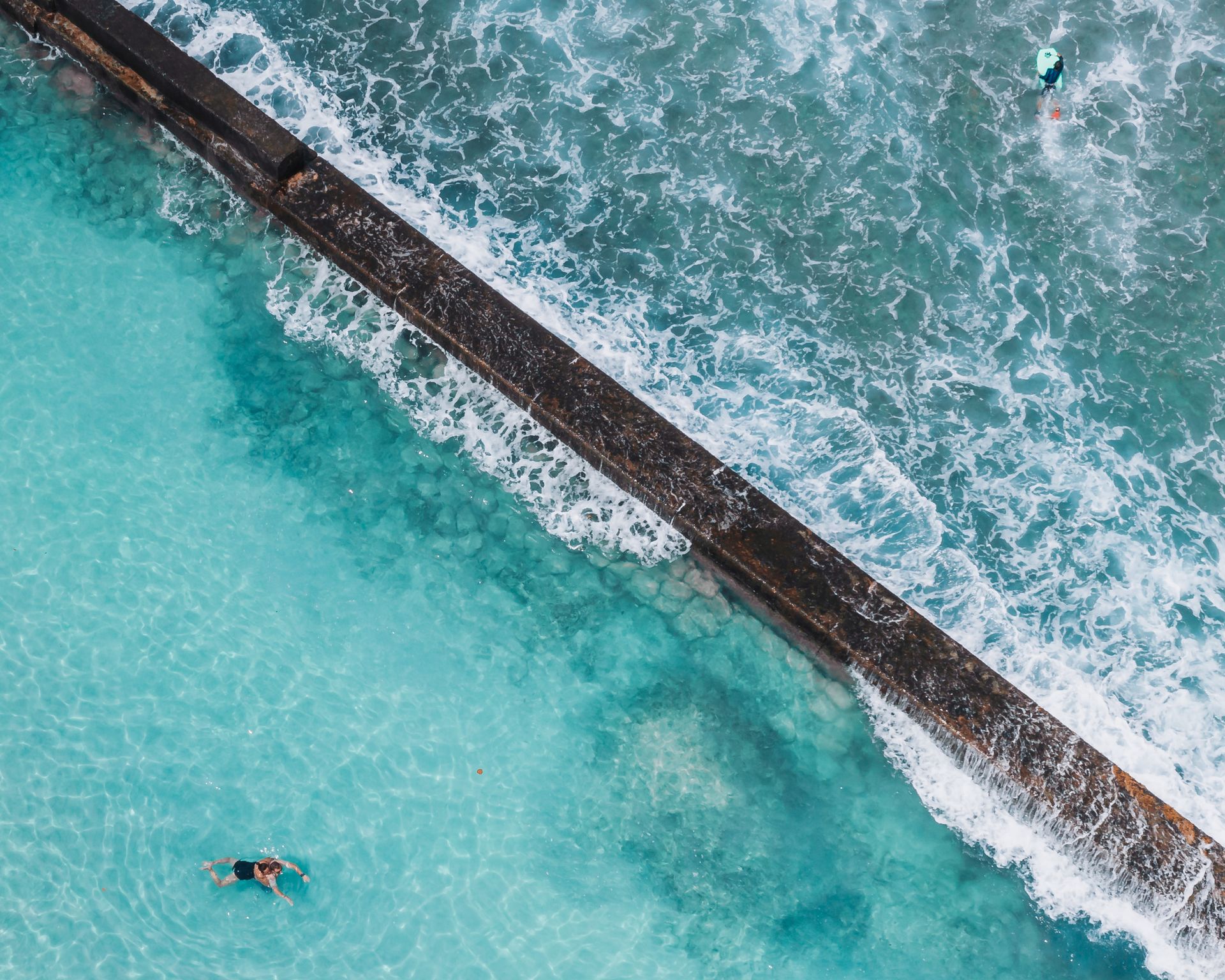 Stunning aerial view of an ocean pool in Hawaii with clear blue waters and ocean waves crashing nearby.
