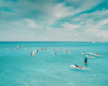 Surfers paddle in turquoise waters off Honolulu's coast under a clear sky.