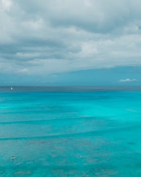 Aerial shot of vibrant turquoise ocean waters with scattered clouds and distant horizon.