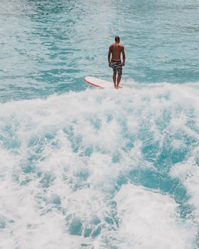 Surfer stands on surfboard amidst azure ocean waves, embodying adventure.