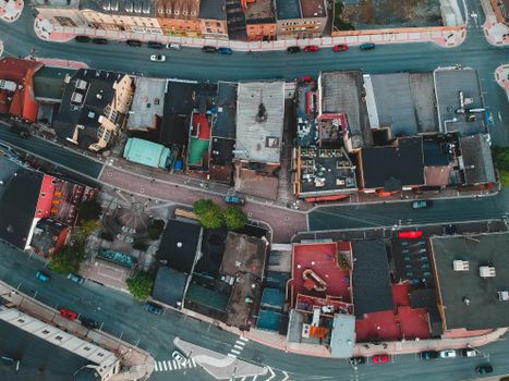 Aerial view of roofs of aged dwelling buildings near asphalt roadways with driving cars in town