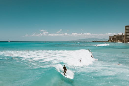 Aerial view capturing surfers riding waves off the coast of Honolulu, with city skyline in the background.