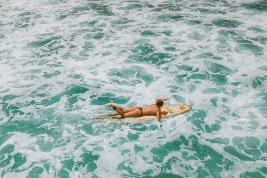 A surfer paddles through vibrant blue waves in Honolulu, captured from above.