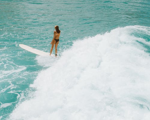 Woman in Black Bikini Standing on White Surfboard on Sea Waves