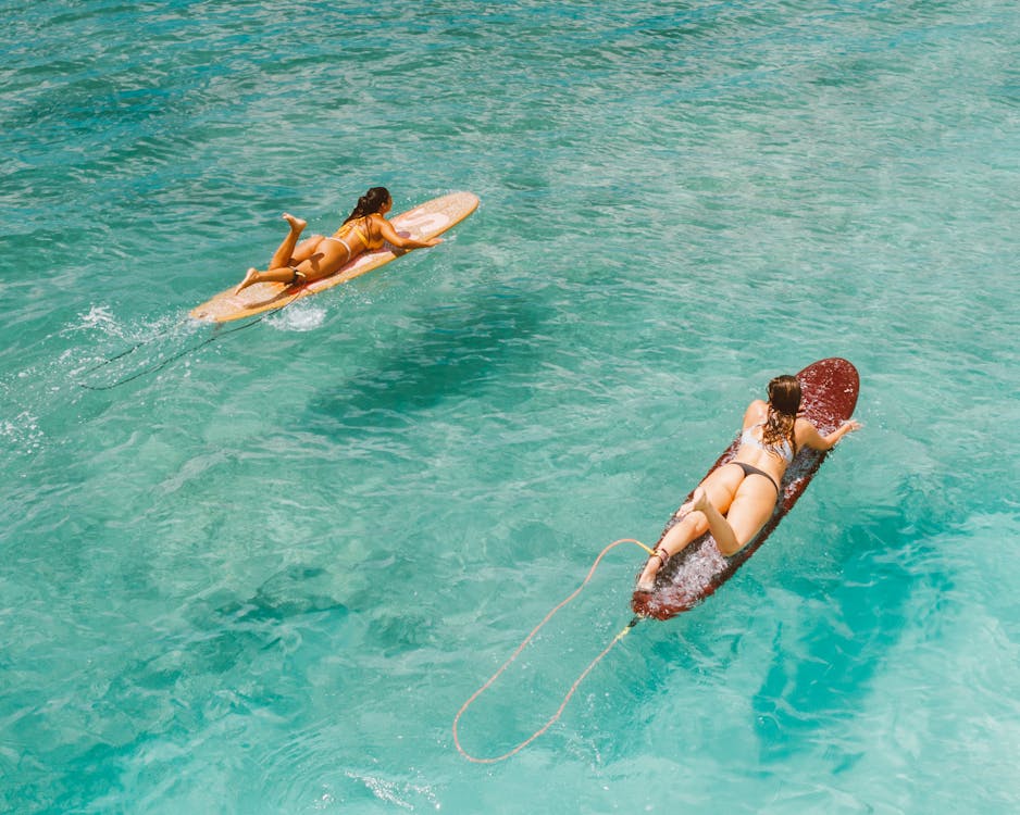 Woman in Black Bikini Lying on Brown Surfboard on Water