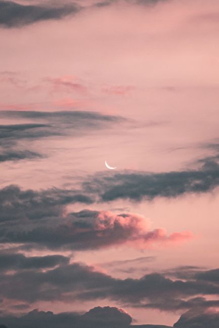 Soft pink and gray evening sky featuring a crescent moon and scattered clouds.