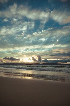 Spectacular view of glowing cloudy sky above mountains and ocean near sandy shore in twilight