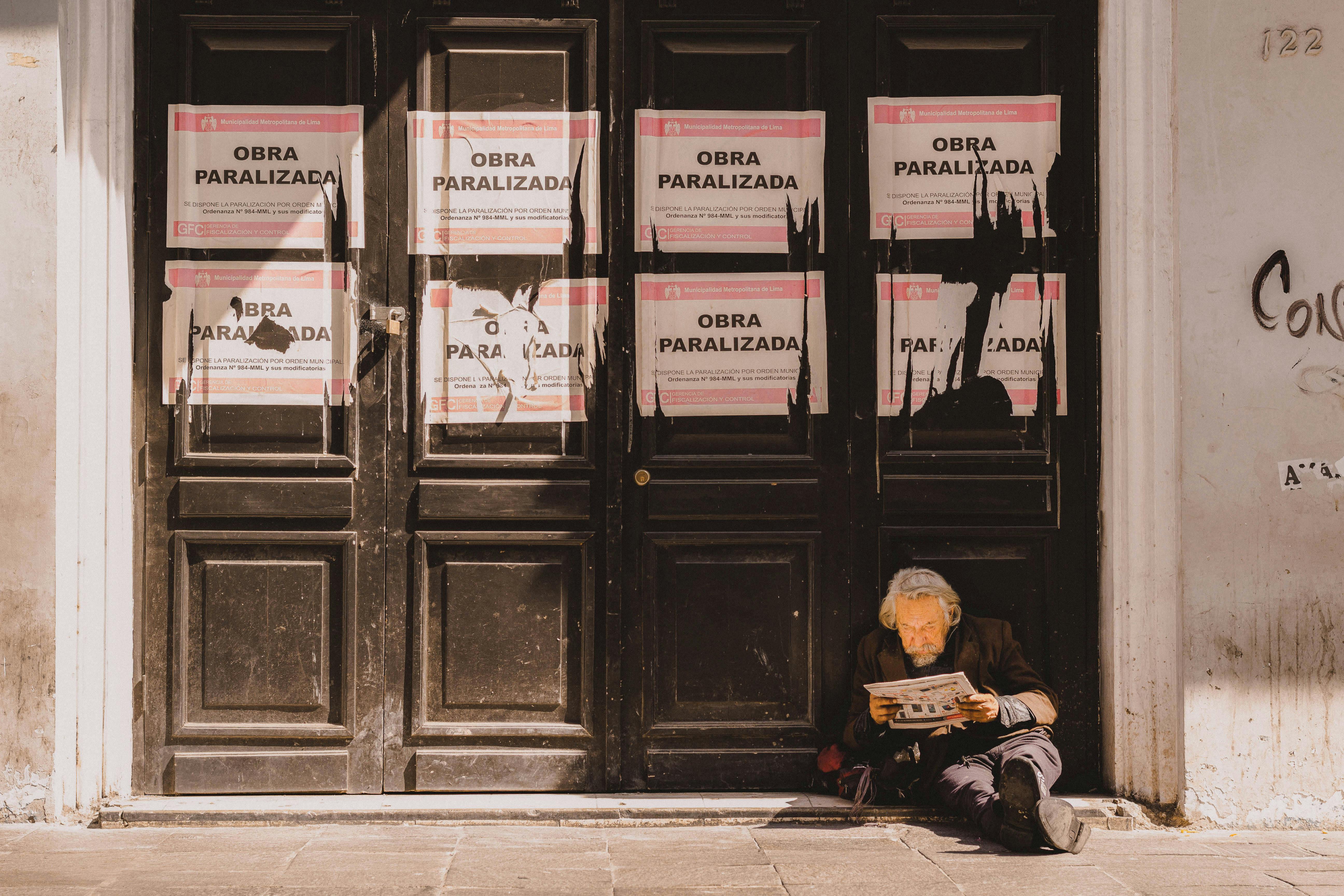 Senior man reading a newspaper against a closed storefront with signs in Lima, Peru.