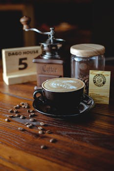 From above of cup with tasty hot drink on wooden table with coffee mill and glass jar