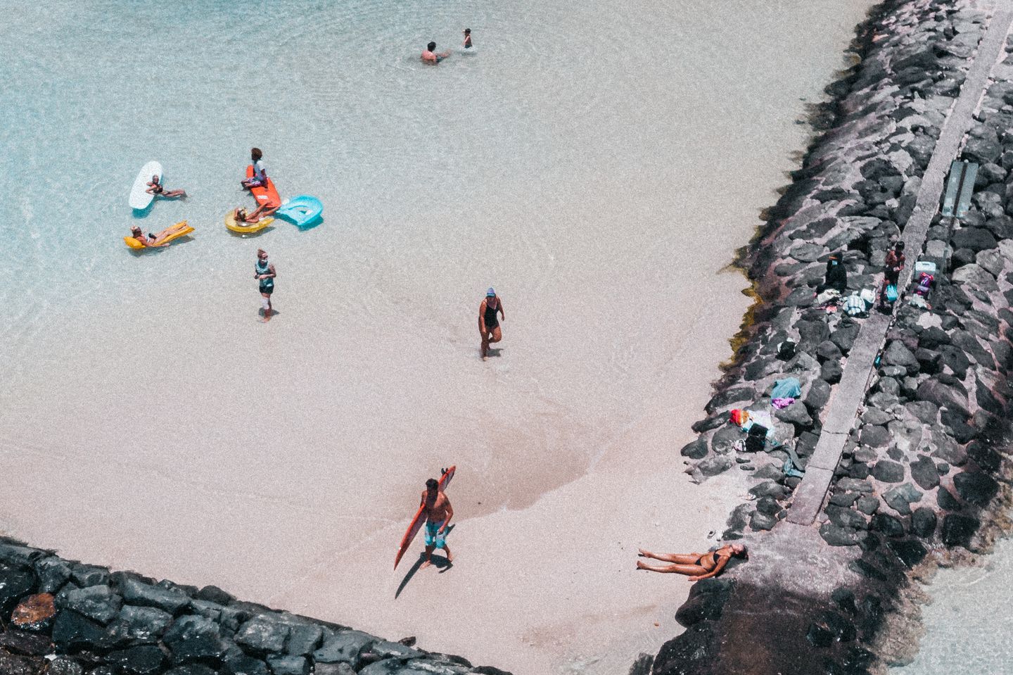 Families spread along a sandy Hawaiian beach with calm shallow water, seen from above