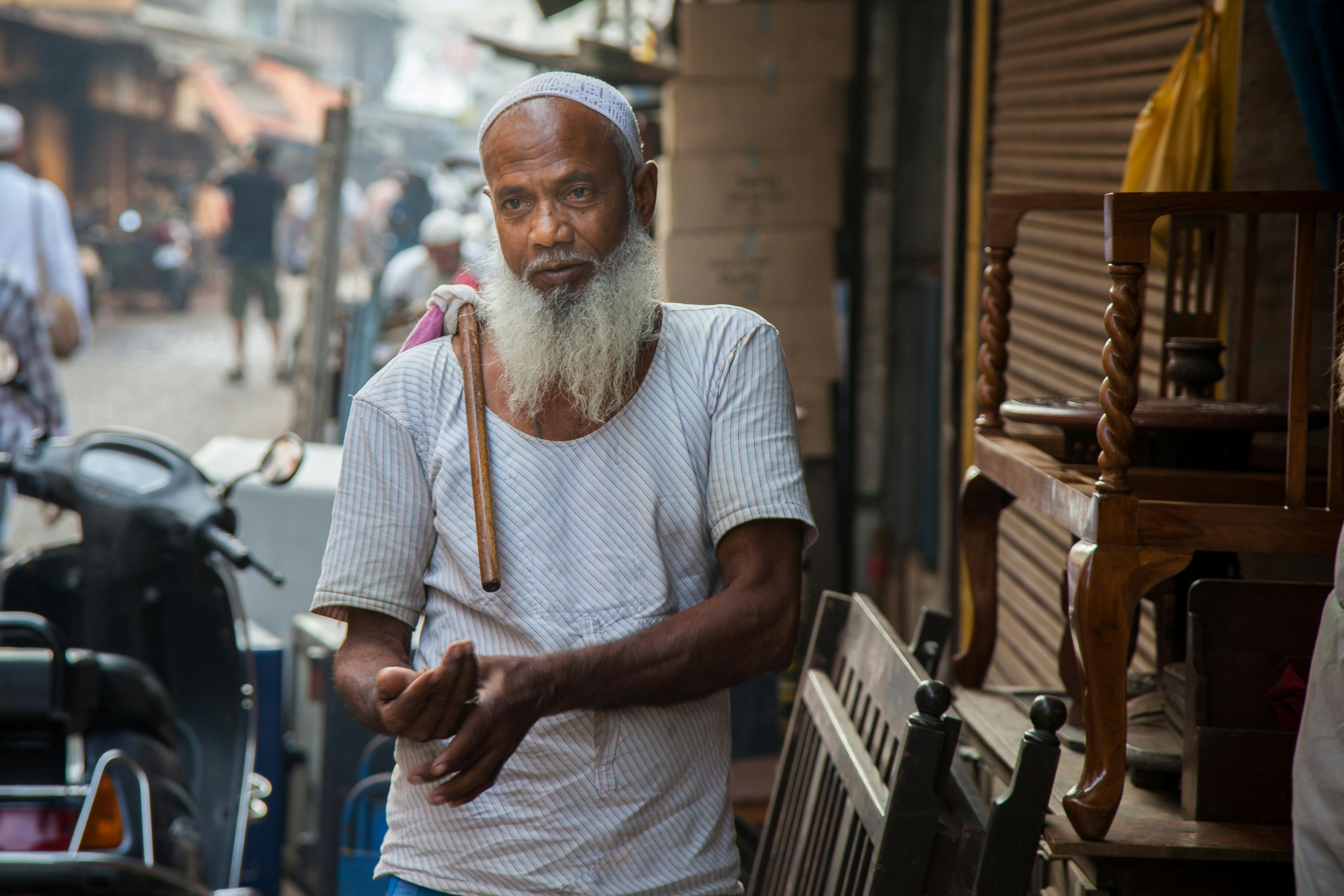 An elderly man with a beard in a busy market in Mumbai's Chor Bazaar, India.