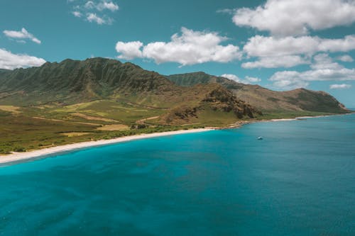 Brown and Green Mountains Beside Blue Sea Under Blue Sky with White Clouds