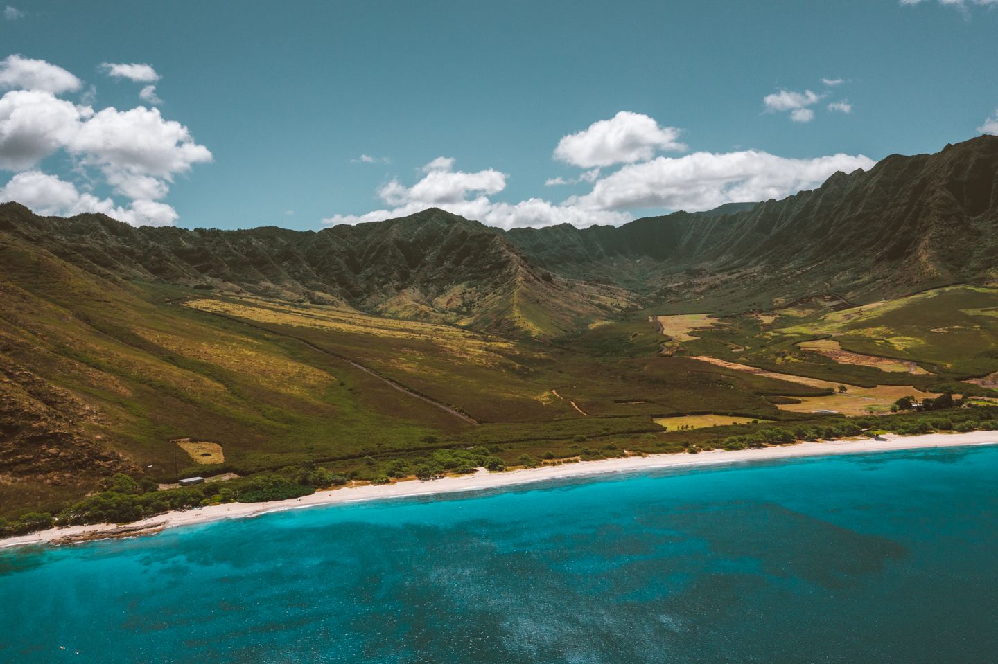 Green Hawaiian mountains dropping to turquoise ocean, seen from the air