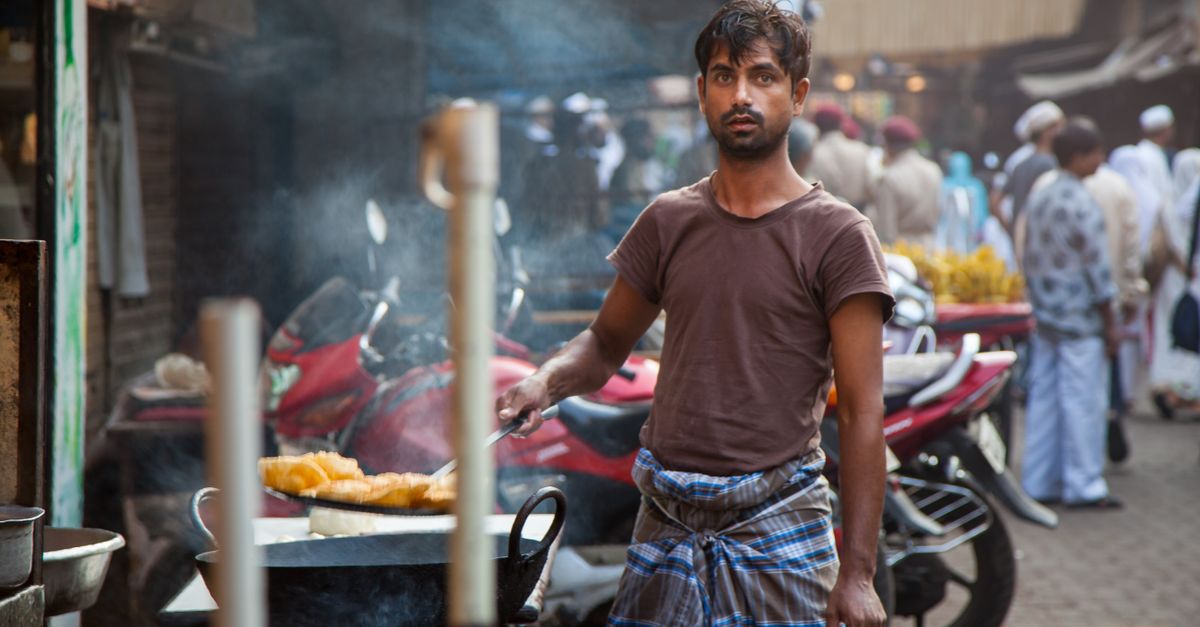 Busy Mumbai street food scene at night with vendors cooking under bright lights and customers crowding around