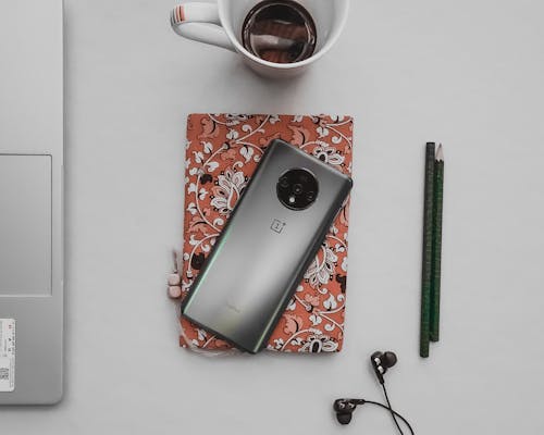 Top view of contemporary cellphone on diary near earphones and pencils with cup of coffee