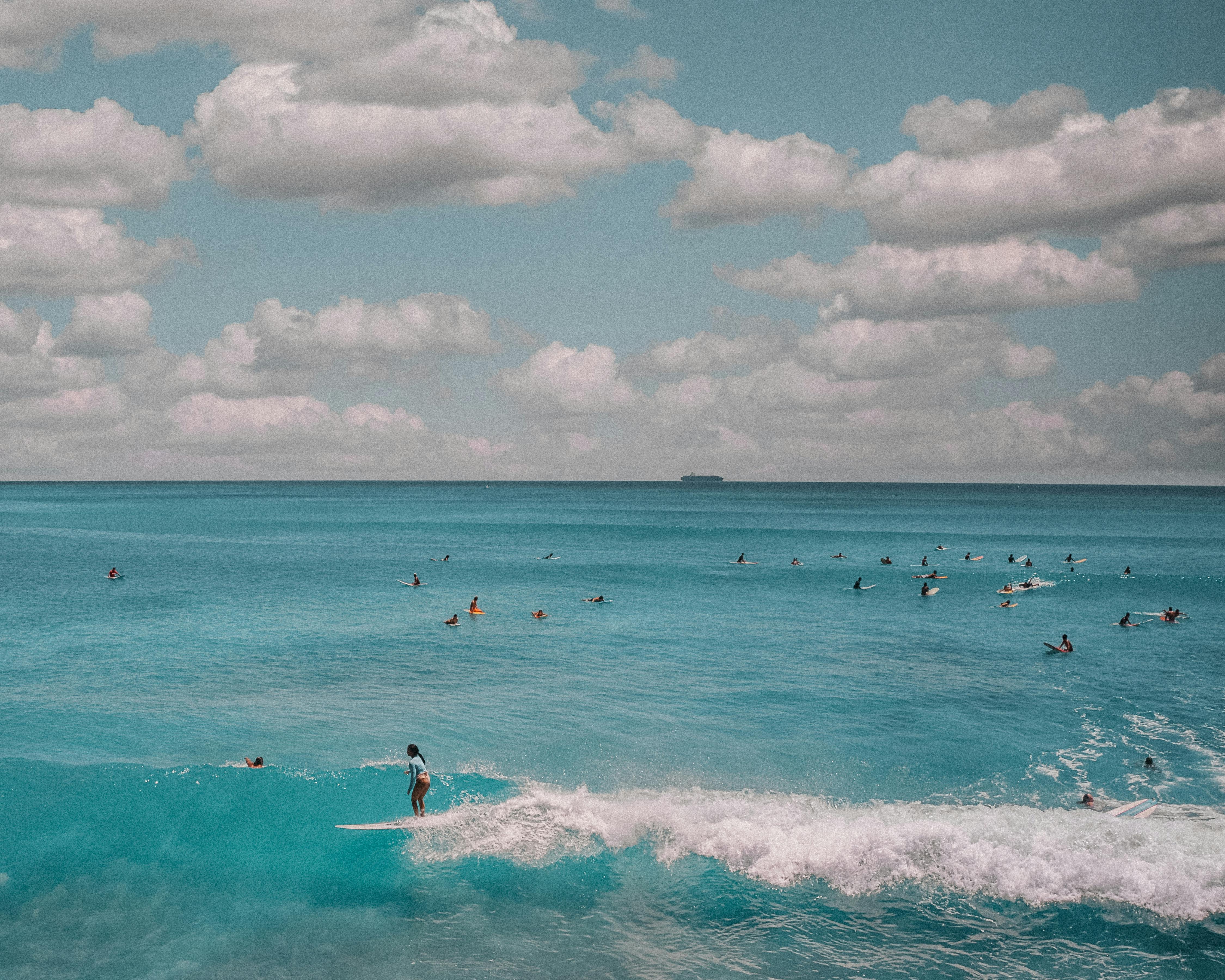 people surfing on sea waves under white clouds and blue sky