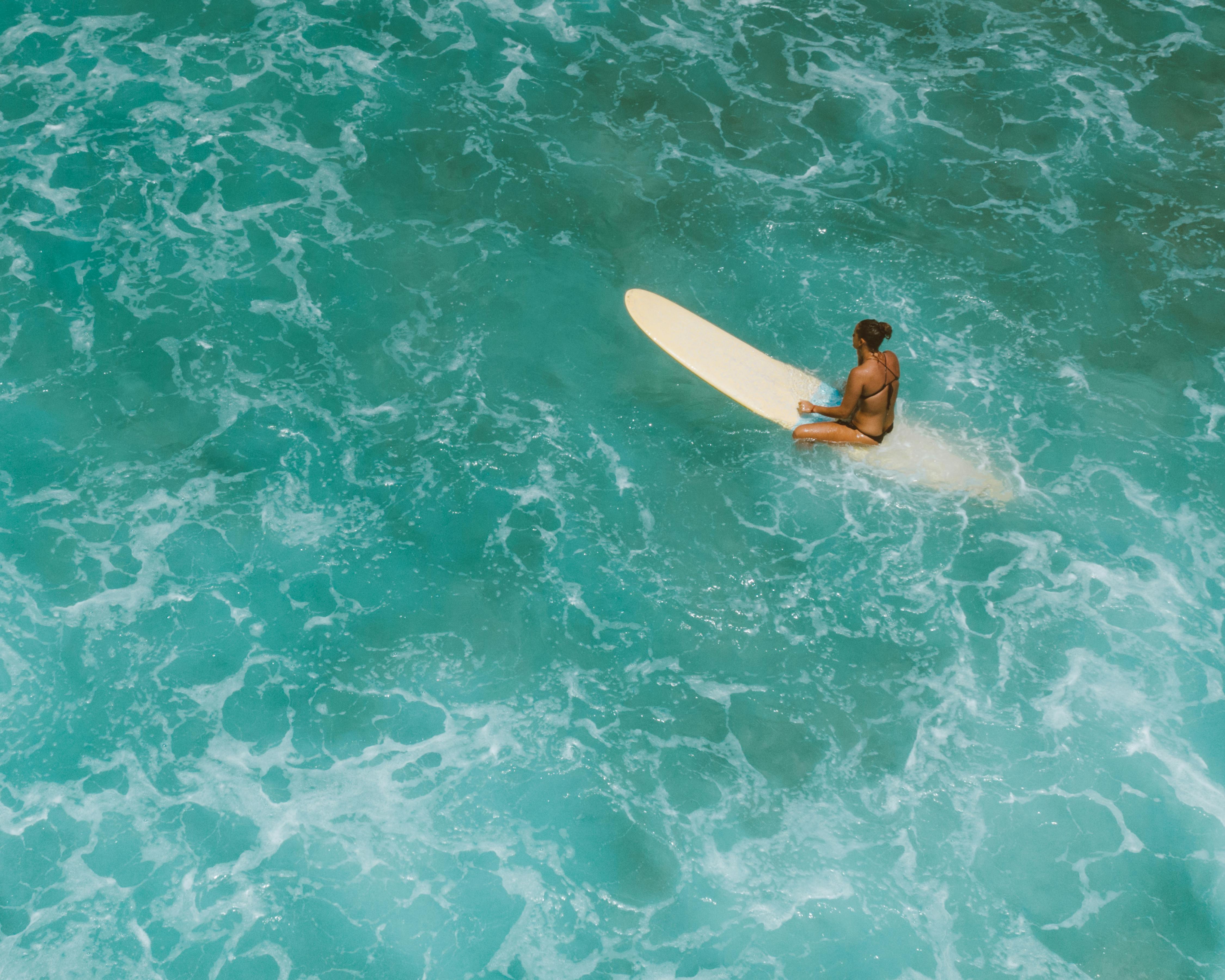 woman in black bikini lying on white surfboard on water