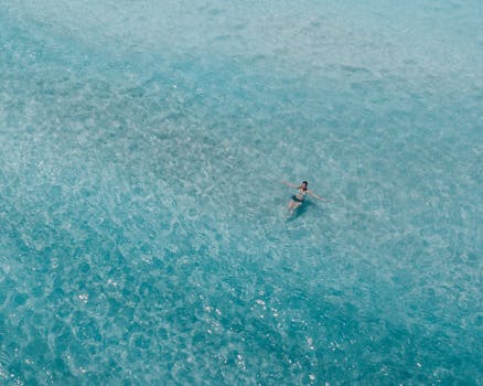 Aerial shot of a woman swimming in the crystal-clear ocean in Hawaii, perfect for summer and vacation themes.