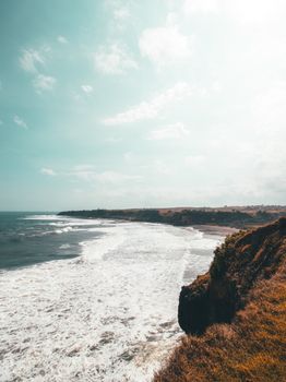 在西爪哇的海岸，明亮的天空下，海浪拍打着悬崖，景色令人惊叹
