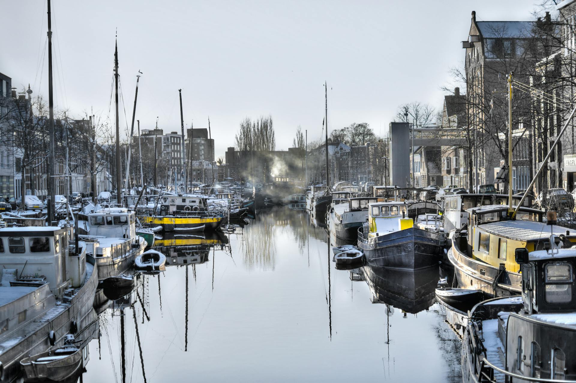 A serene, snow-dusted harbor scene featuring numerous boats docked along a calm waterway.