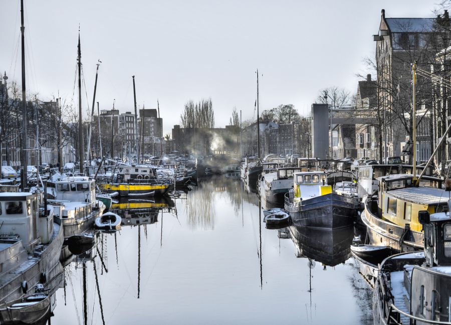 A serene, snow-dusted harbor scene featuring numerous boats docked along a calm waterway.