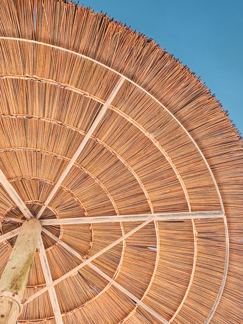 Free Low-angle view of a bamboo beach umbrella set against a clear blue sky, capturing the essence of summer relaxation. Stock Photo