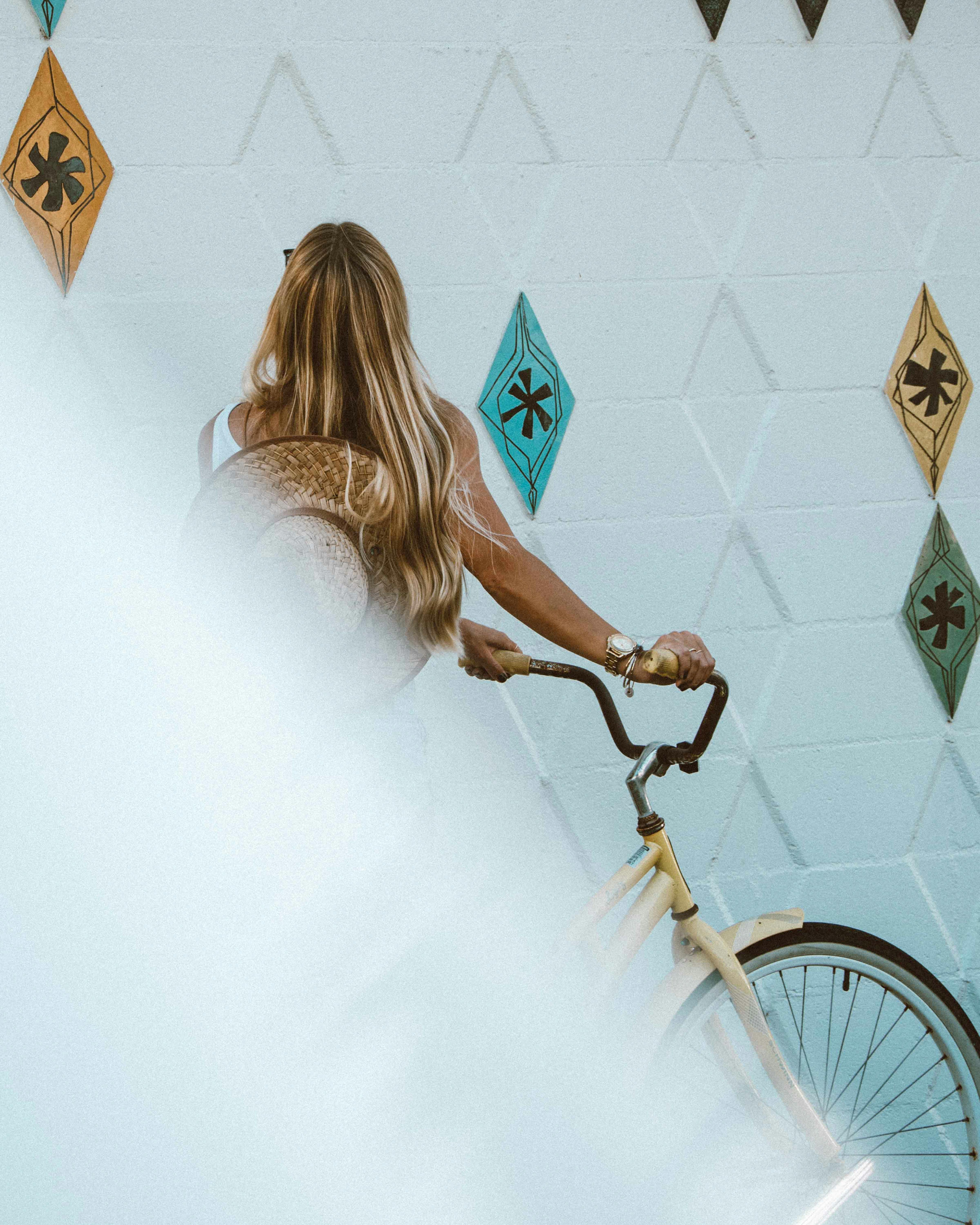 一名金发女子骑着自行车，停在户外的几何图案墙壁前
