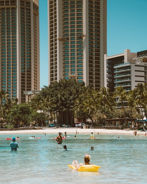 People Swimming on Beach Near High Rise Buildings