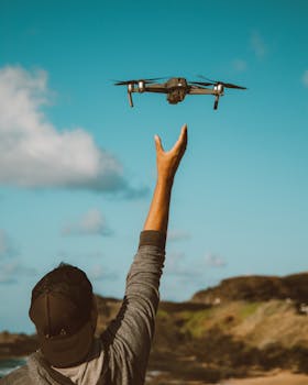A person operates a drone outdoors under a clear blue sky by the coast.